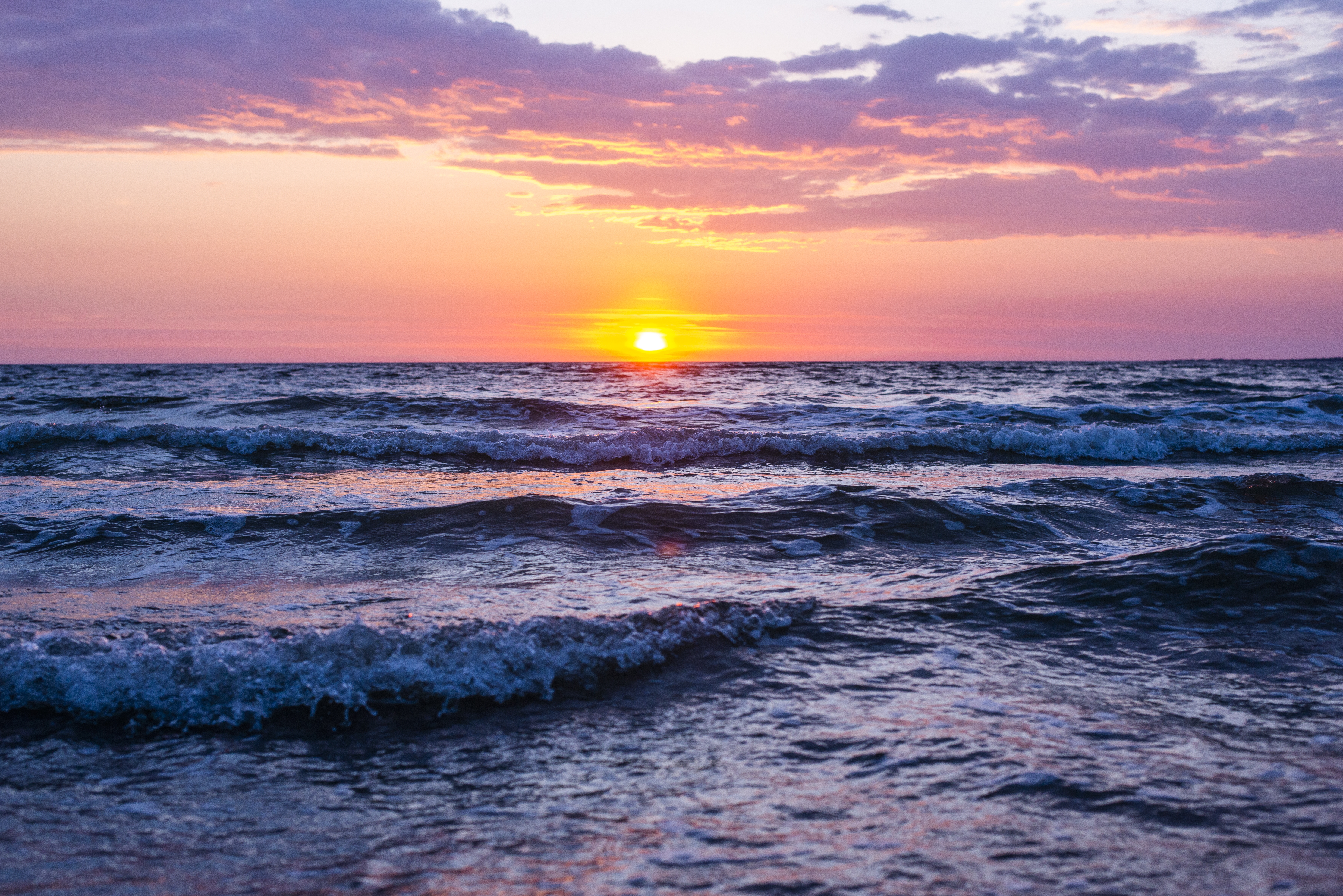 23+ Ways to Reduce Anxiety and Stress (in no particular order) A sun shining during golden hour with pink and purple cloud colors and sea waves